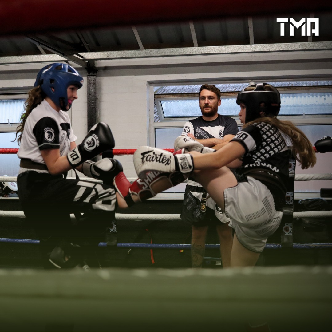 Two Trojan Martial Arts students sparring in the ring while a coach watches